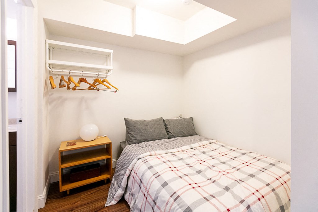 A bedroom with a bed, pillows, a nightstand, and a hanging closet.