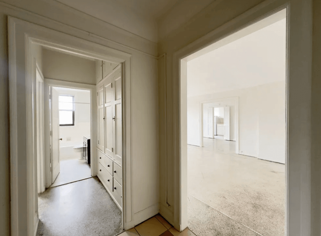 A hallway with a door on the left and a room on the right.