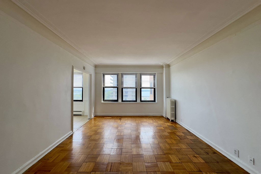 A room with wooden flooring and three windows.