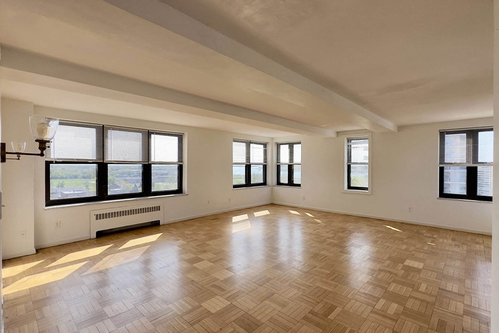 A large empty room with wooden flooring and windows.