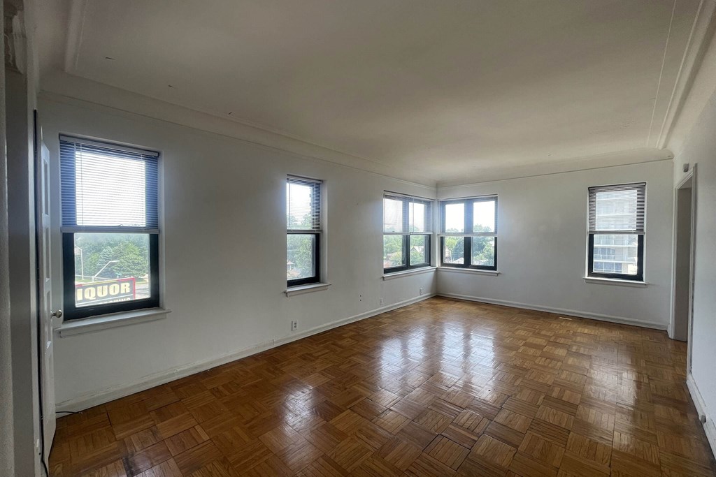 Empty room with wooden flooring and windows.