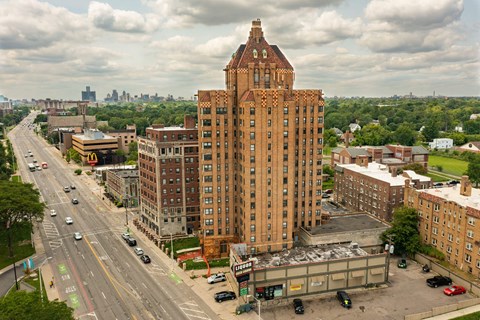 A tall brown building with a pointed top is in the middle of a city street.