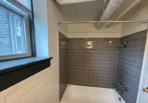 A bathroom with a white tub and grey tiled walls.