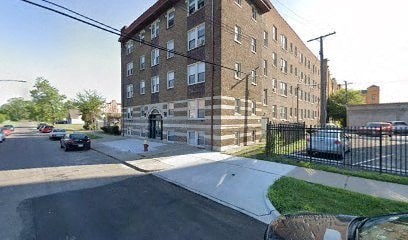 A street view of a residential area with a brick building on the left and cars parked on the side of the road.