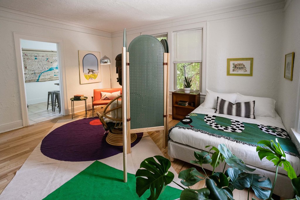 A bedroom with a bed, a chair, a table, and a green rug.