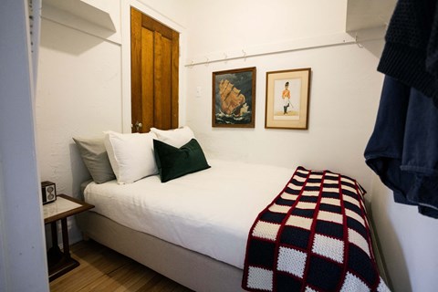 A bedroom with a bed, pillows, a blanket, a nightstand, and two pictures on the wall.