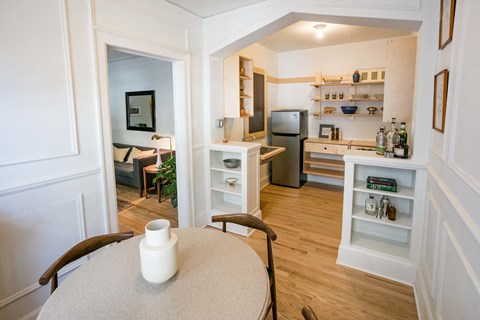 A kitchen with a refrigerator, sink, and a dining table with a vase on it.