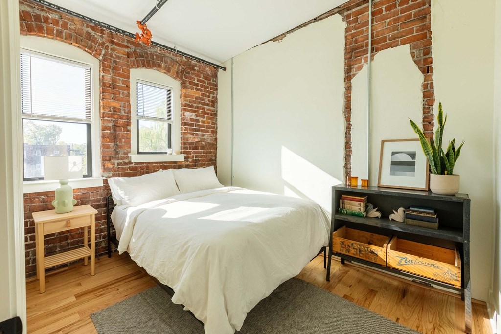 A bedroom with a bed, nightstand, and a brick wall.