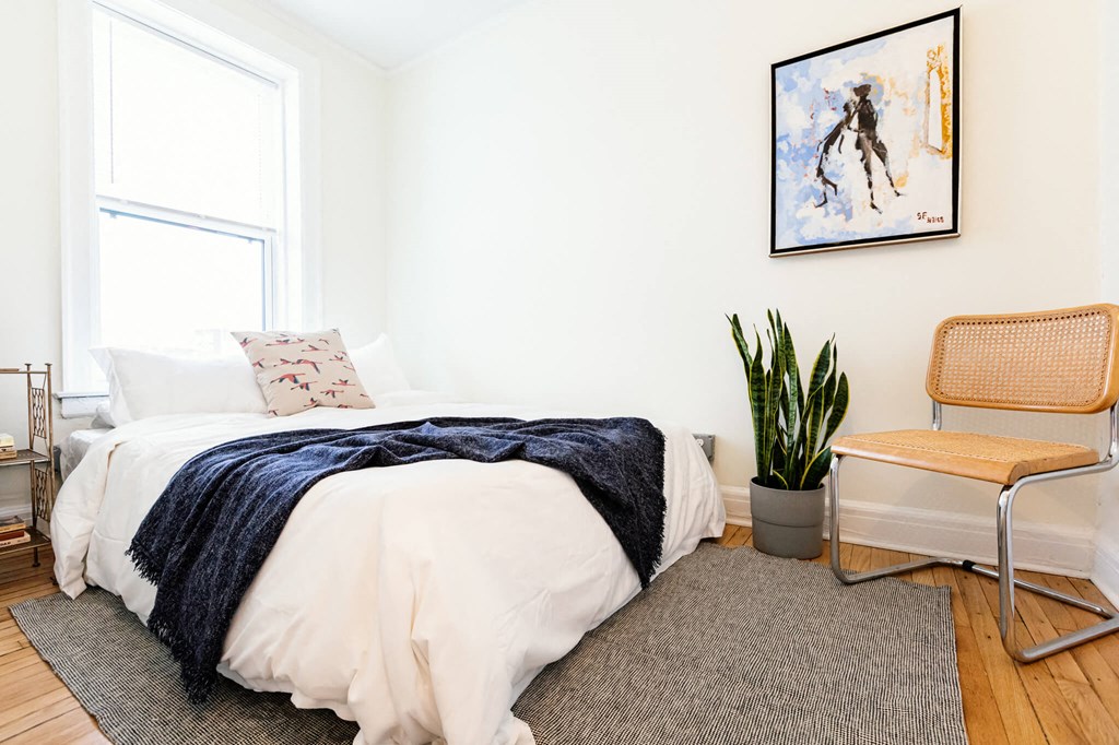 A bedroom with a bed, chair, and a painting on the wall.