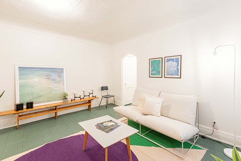 A living room with a white couch and a painting on the wall.