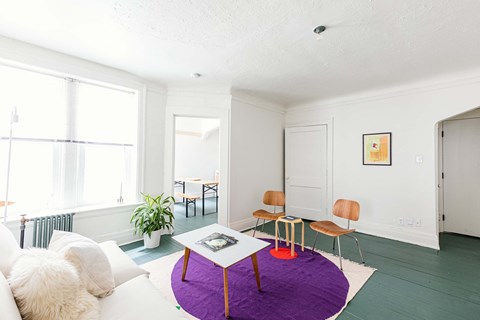 A white couch with a purple ottoman in front of a table with chairs.