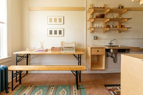 A kitchen with a table and chairs and a shelf with various items on it.