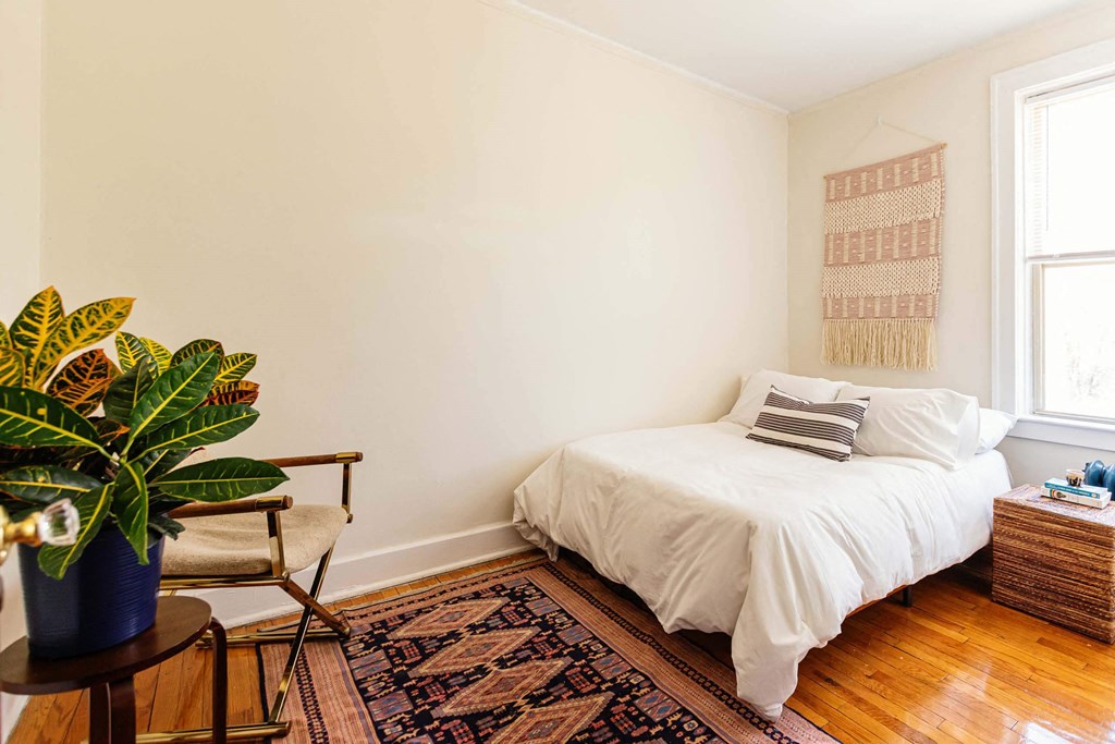A bedroom with a white bed and a plant on a side table.