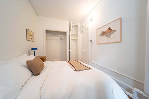 A bedroom with a white bed and a painting on the wall.