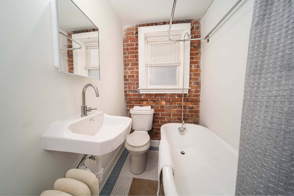 A white sink is on the left of a white toilet in a bathroom with a brick wall.