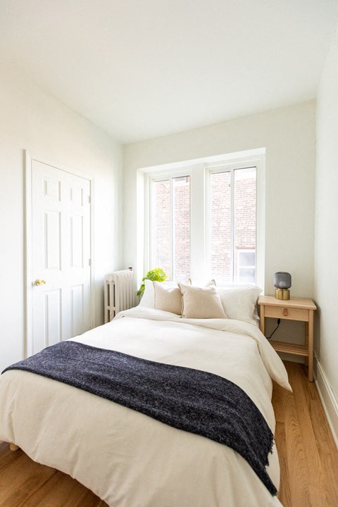 A bedroom with a white bed and a window with a view of a brick building.