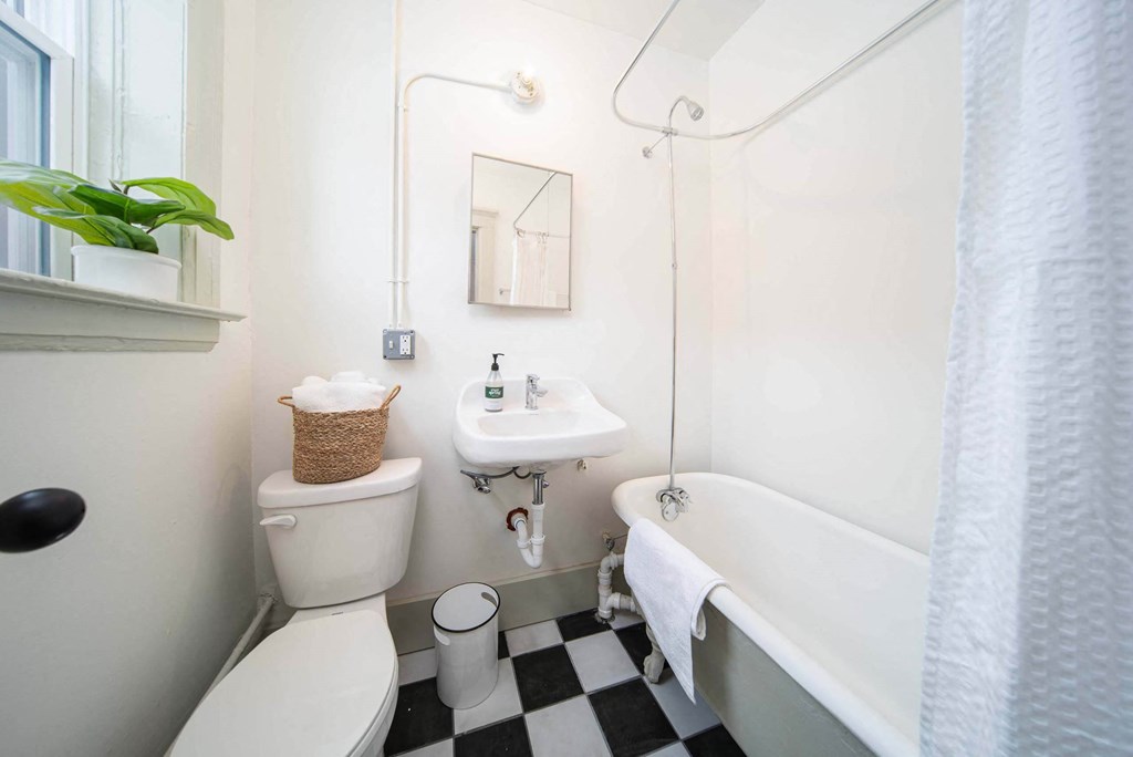 A white toilet with a basket on top sits next to a white sink in a bathroom.