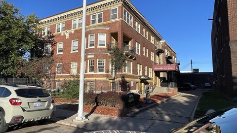 A white car is parked on the side of a street in front of a brick building.