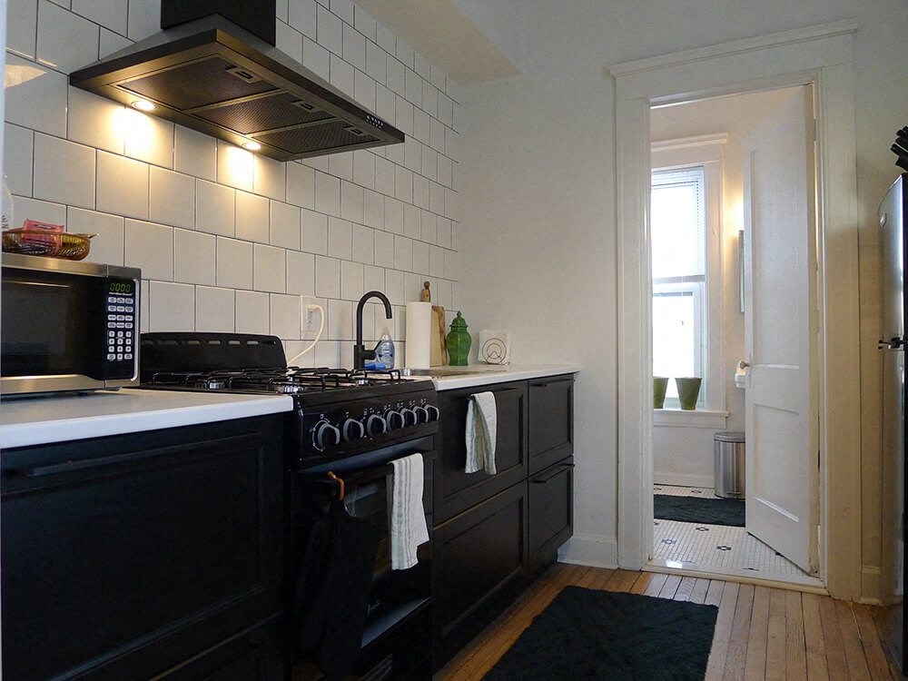 A kitchen with black cabinets and a white tiled wall.