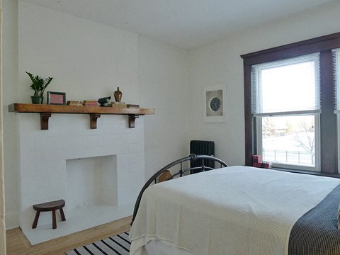 A bedroom with a bed, a fireplace, and a window.