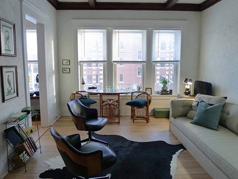 A living room with a black and white cowhide rug, a black leather chair, a grey couch, and a wooden floor.