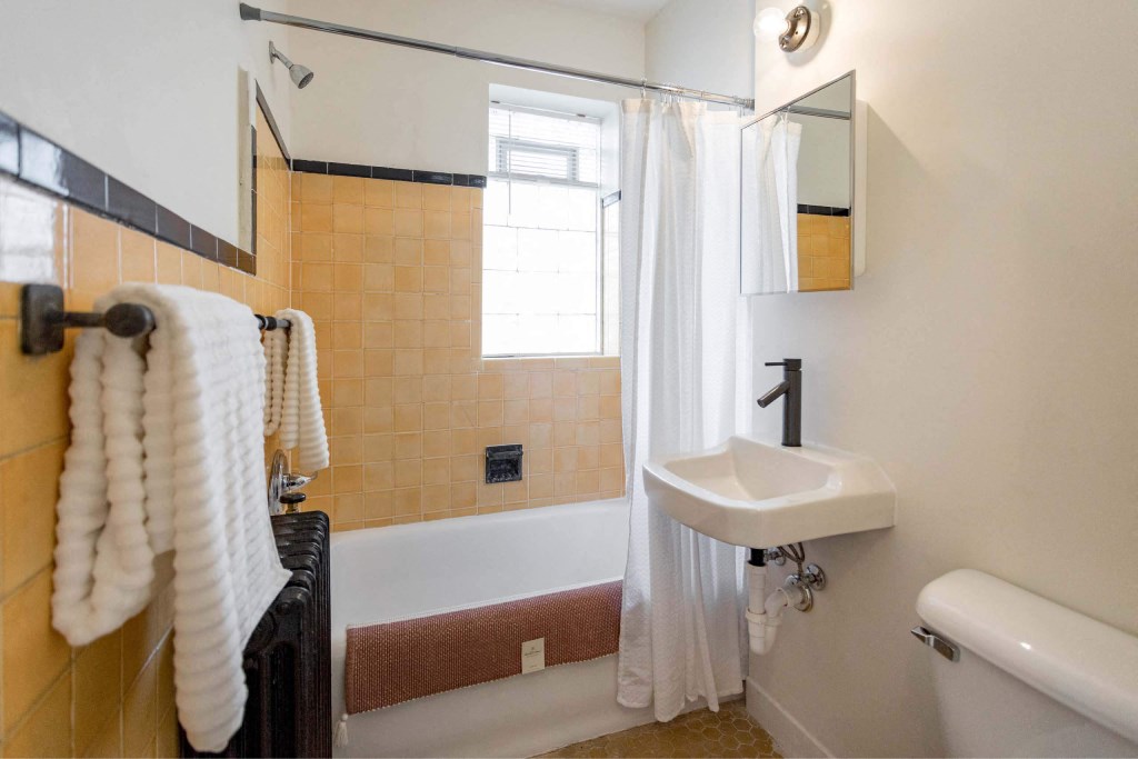 A bathroom with a white sink and a bathtub with a brown mat.