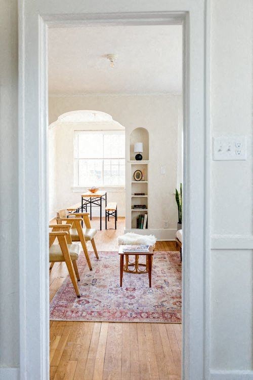 A room with a white door, a table with chairs, a rug, and a bookshelf.