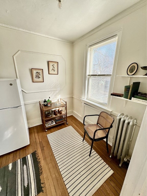 A room with a white refrigerator, a chair, a table with bottles and a shelf with books.