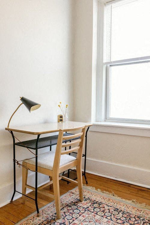 A desk with a chair and a lamp on a patterned rug.