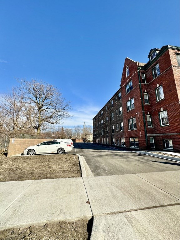 A white car is parked on a concrete driveway in front of a red brick building.