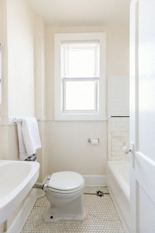 A white toilet in a bathroom with a white tub and a window.