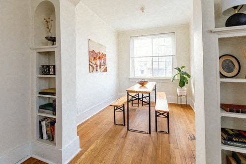 A room with a wooden floor, a table with chairs, and a bookshelf filled with books.