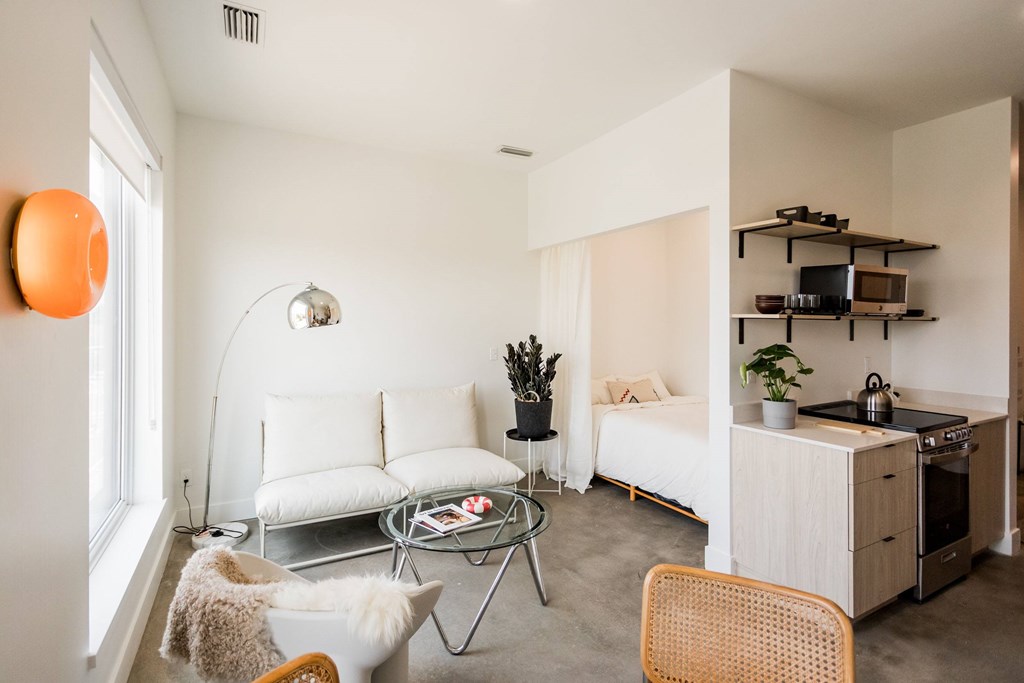A modern living room with a white couch, a glass coffee table, and a kitchen area in the background.