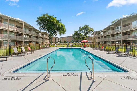 A swimming pool in a residential area with lounge chairs and trees.