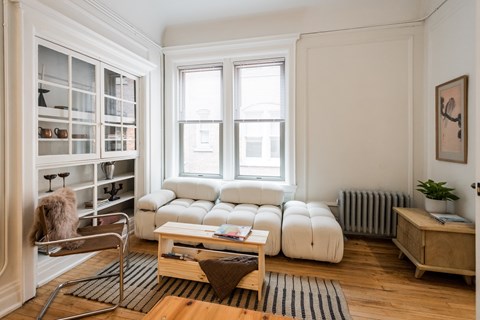 A living room with a white couch, a wooden coffee table, and a window with blinds.