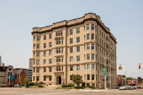 A large, beige building with many windows sits on a street corner.