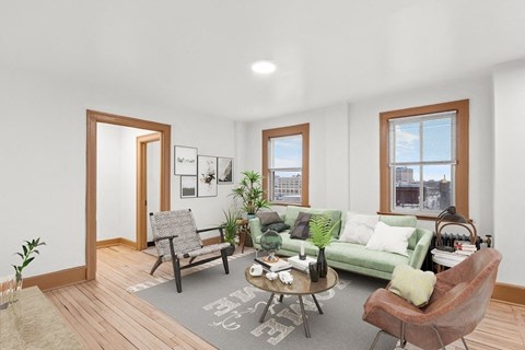 A living room with a green couch, a grey armchair, a wooden floor, and a grey rug with a white design.