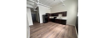 A kitchen area with wooden flooring and a black refrigerator.