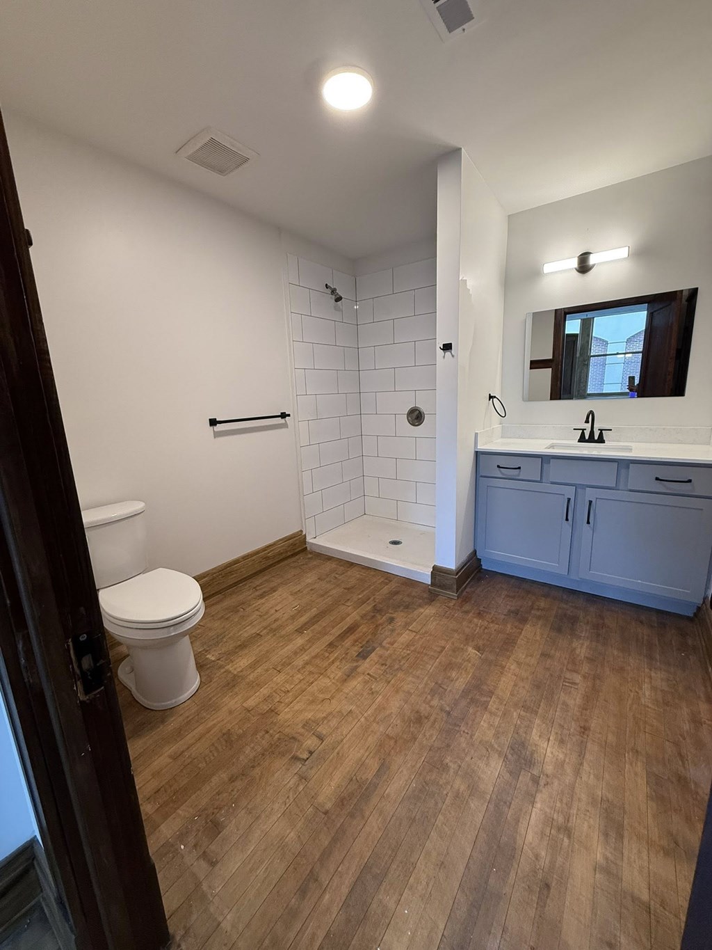 A bathroom with a toilet, sink, and wooden floor.