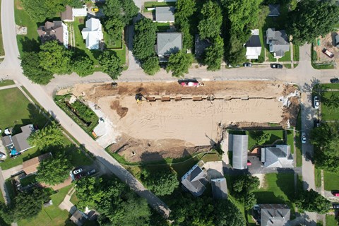 A construction site is surrounded by houses and trees.