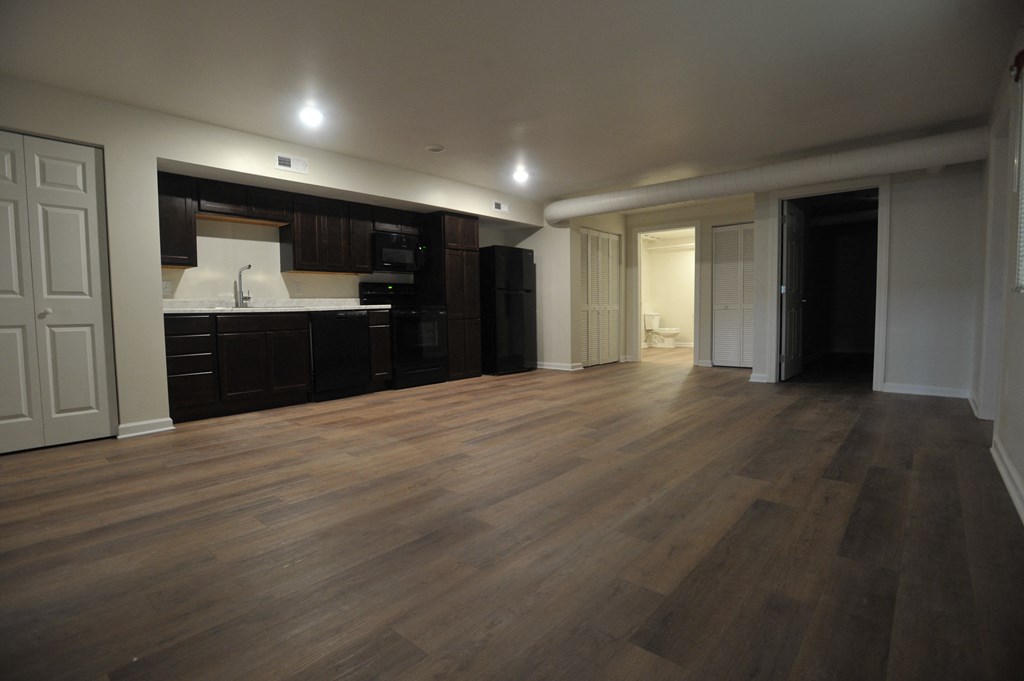 an empty living room with wooden floors and a kitchen