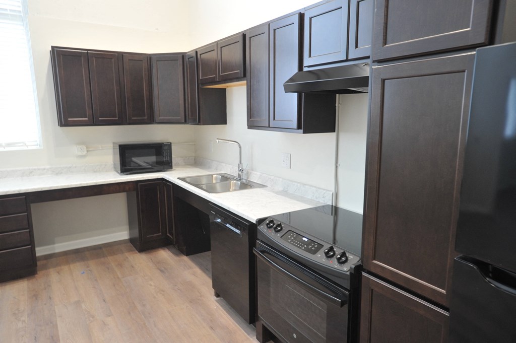 an empty kitchen with dark wood cabinets and white counter tops and a stainless steel sink