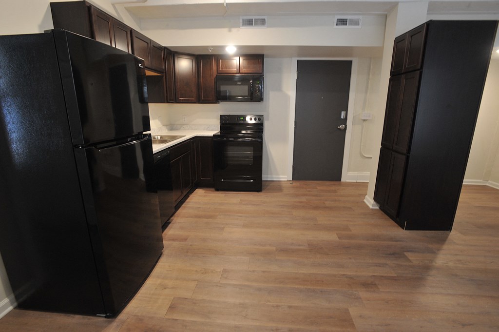 an empty kitchen with black appliances and wooden floors