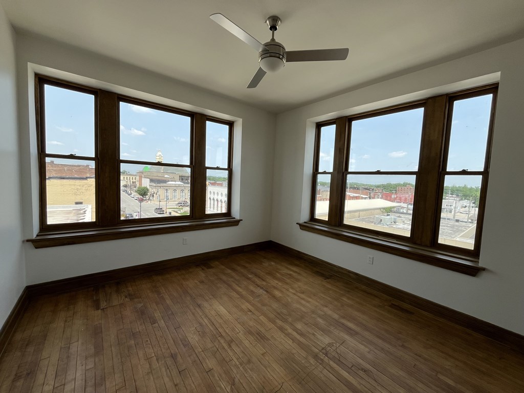 A room with wooden floors and two windows overlooking a parking lot.