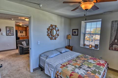 A bedroom with a bed, a chair, a ceiling fan, and a window.