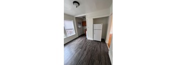 A room with a white fridge and wooden floors.