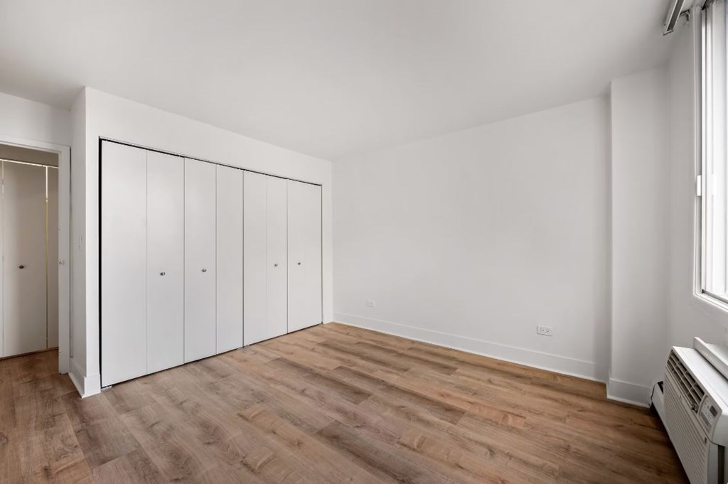 A room with white walls and wooden flooring with a window on the right side.