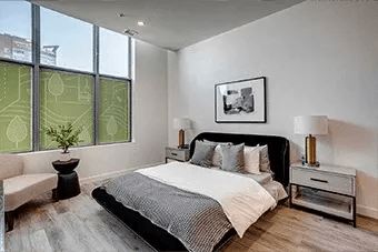 A bedroom with a large bed, a nightstand, and a window with a view of a building outside.