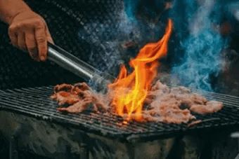 A person is grilling meat with a flame.
