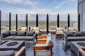 A patio with grey couches and wooden chairs overlooking a cityscape.